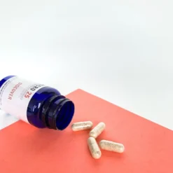 Close up of uniform clear vegetable capsules filled with a finely ground Discover blend botanical powder beside a bottle