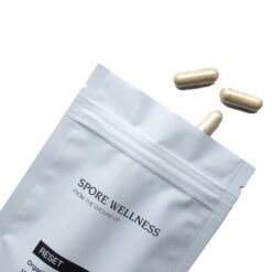 Spore Wellness brand Reset container standing next to several two piece vegetable capsules